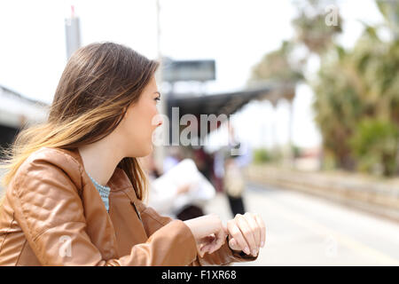 Arrabbiato ragazza in attesa in una stazione ferroviaria e alla ricerca per la linea ferroviaria Foto Stock