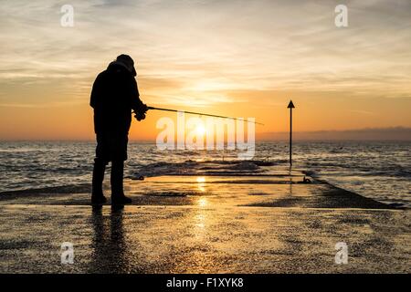 Francia, Finisterre, Fouesnant, Pointe de Mousterlin, pescatore sul molo al tramonto Foto Stock