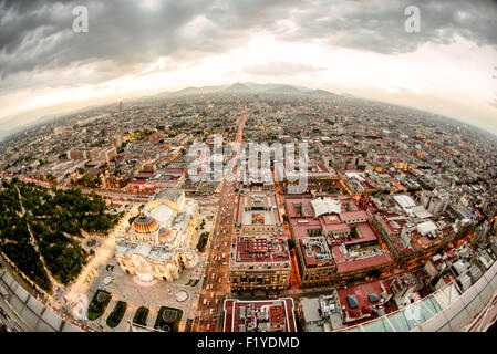 Vista aerea del Palacio de Bellas Artes Dusk di città del Messico | CITTÀ DEL MESSICO, Messico - il tramonto si adagia sul Centro Histórico mentre la cupola dorata del Palacio de Bellas Artes cattura l'ultima luce in questa vista aerea fisheye dalla Torre Latinoamericana, con il baldacchino di Alameda Central che si estende sotto e la Sierra de las Cruces all'orizzonte. L'architetto italiano Adamo Boari iniziò il palazzo nel 1904; Federico Mariscal lo completò nel 1934, lasciando un esterno Art Nouveau su un interno Art Deco. Foto Stock
