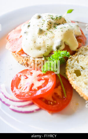 Uova Benedict con verdure fresche a fette e bagel su una piastra bianca Foto Stock