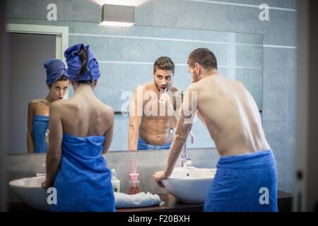 Vista posteriore della coppia giovane spazzolare i denti in Specchio bagno Foto Stock