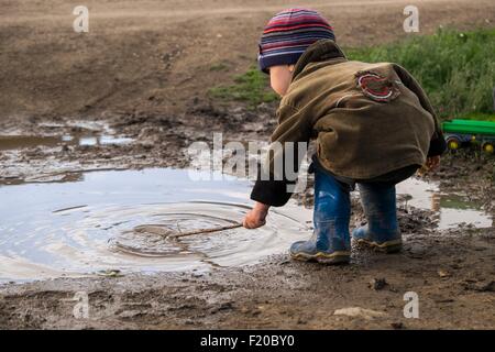 Bimbi maschi di indossare stivali di gomma giocando con il bastone di Pozza Foto Stock