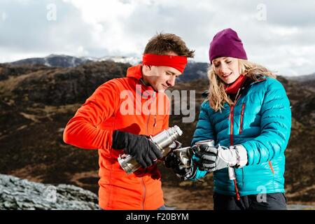 Coppia giovane prendendo una pausa da escursionismo, avente una bevanda calda, Honister miniera di ardesia, Keswick, Lake District, Cumbria, Regno Unito Foto Stock