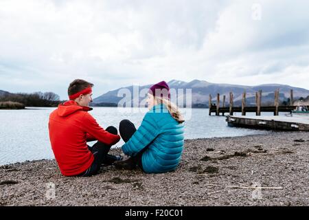 Coppia giovane escursionismo, seduta da Waters Edge, Derwent Water, Keswick, Lake District, Cumbria, Regno Unito Foto Stock