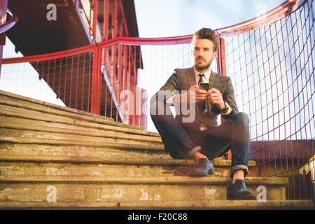 Elegante giovane uomo seduto su passerella scale con lo smartphone Foto Stock