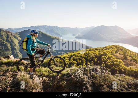 Giovane donna in mountain bike, guardando a vista, Lago di Como, Italia Foto Stock