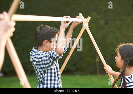 Fratello e Sorella mettendo in casa tenda telaio in giardino Foto Stock