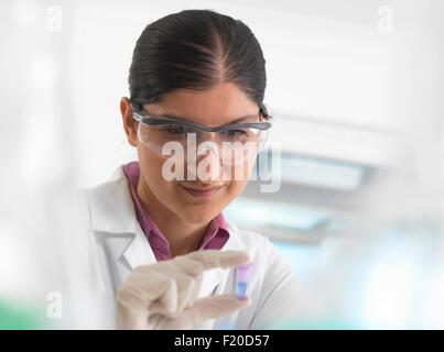 Donna scienziato visualizzazione di campione nella provetta eppendorf davanti a DNA testing in laboratorio. Foto Stock