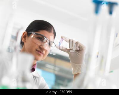 Donna scienziato visualizzazione di campione nella provetta eppendorf davanti a DNA testing in laboratorio. Foto Stock