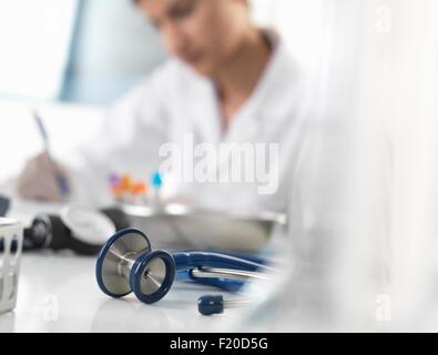 Medico donna scrivendo documentazione medica alla scrivania in clinica Foto Stock