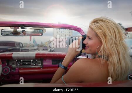 Giovane donna di scattare le foto da un'auto d'epoca sul' Havana Malecon, Cuba Foto Stock