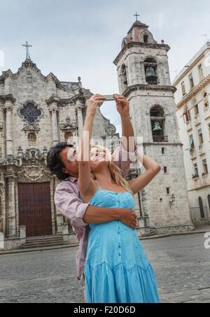 Coppia giovane tenendo selfie con lo smartphone nella Plaza de la Cattedrale de L Avana, Cuba Foto Stock