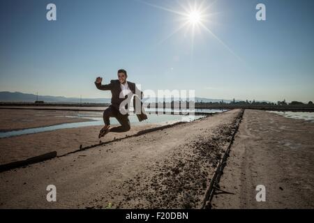 Adulto medio imprenditore valigetta porta jumping metà aria a spiaggia Foto Stock