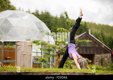 Donna matura la pratica dello yoga con una gamba sollevata in eco lodge garden Foto Stock