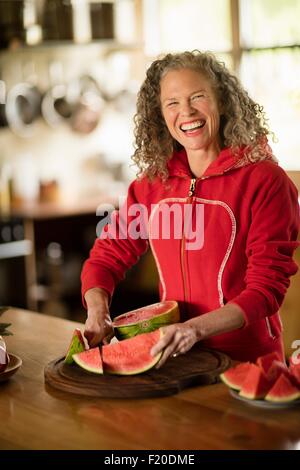 Ritratto di donna matura per affettare cocomero in cucina Foto Stock