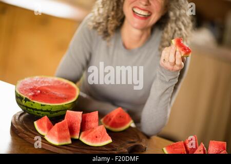 Donna matura mangiando anguria in cucina Foto Stock