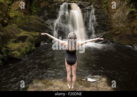 Vista posteriore della donna matura la pratica con le braccia aperte davanti a cascata Foto Stock