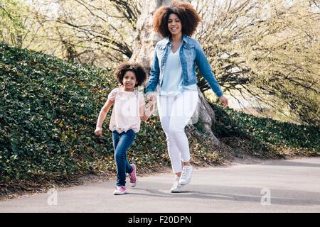 A piena lunghezza shot di madre e figlia per mano camminando lungo il sentiero sorridente Foto Stock