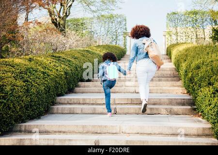 Vista posteriore della madre e figlia per mano salendo le scale Foto Stock