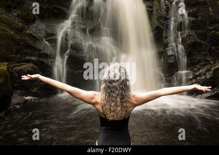 Vista posteriore della donna matura la pratica dello yoga pongono di fronte a cascata Foto Stock