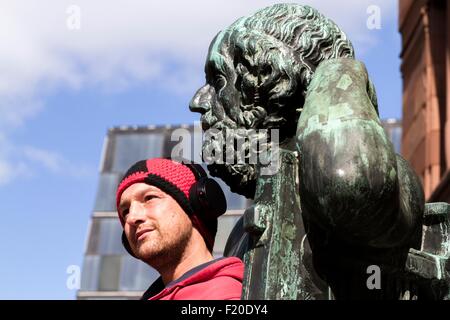 Ritratto di metà uomo adulto che indossano le cuffie nella parte anteriore della scultura, Freiburg, Baden, Germania Foto Stock