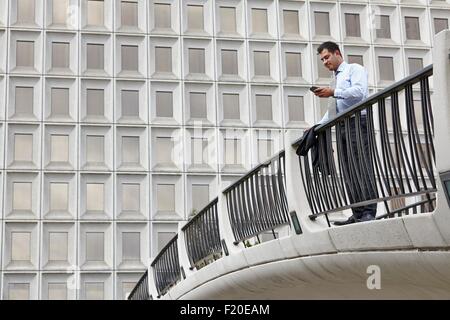 Metà adulto uomo d affari permanente sulla passerella elevata guardando smartphone Foto Stock