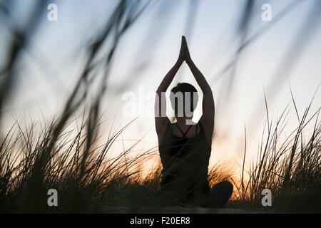 Vista posteriore della metà donna adulta a praticare yoga in stagliano erbe lunghe al tramonto Foto Stock