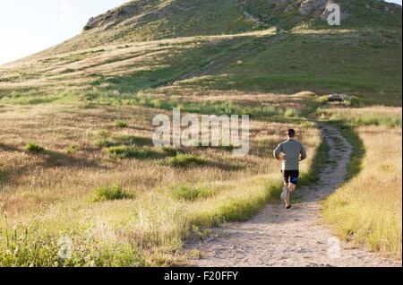 Vista posteriore del giovane maschio runner acceso fino hillside via Foto Stock