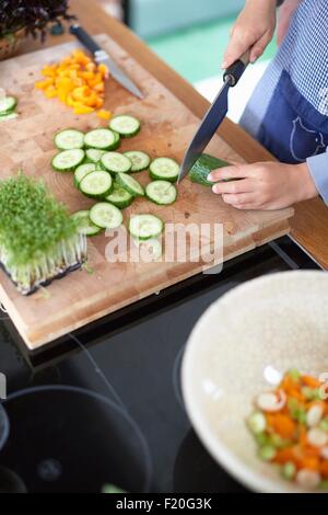 La donna per affettare cetrioli in cucina Foto Stock