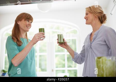 Le donne di bere verde frullato vegano in cucina Foto Stock