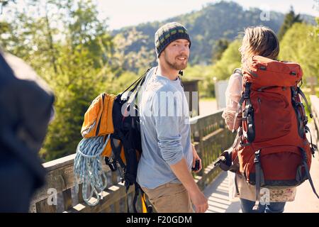Vista posteriore di escursionisti che trasportano zaini, guardando sopra la spalla, sorridente Foto Stock