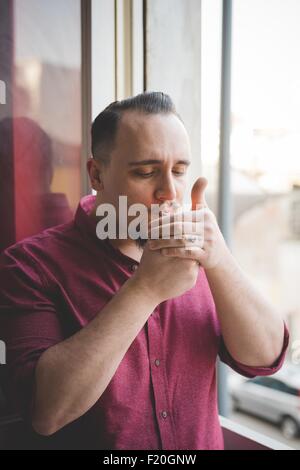 Ritratto di giovane uomo il fumo dalla finestra Foto Stock