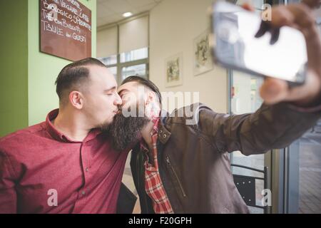 Coppia gay tenendo selfie e baciare in cafe Foto Stock