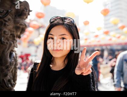 Ritratto di giovane donna con capelli lunghi e occhiali da sole sulla testa facendo segno di pace, guardando la fotocamera Foto Stock