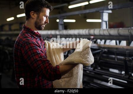 Ritratto di tessitore maschio esaminando laccio dalla vecchia macchina di tessitura nel mulino tessile Foto Stock