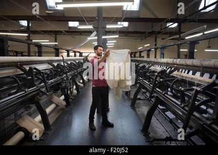 Ritratto di tessitore maschio esaminando il tessuto dalla vecchia macchina di tessitura nel mulino tessile Foto Stock