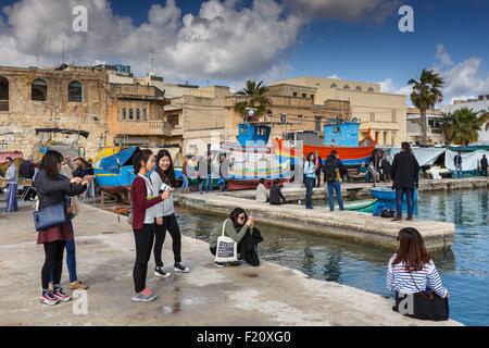 Malta, Marsaxlokk, giapponesi turisti rendendo selfies il bordo dell'acqua in un villaggio di pescatori Foto Stock