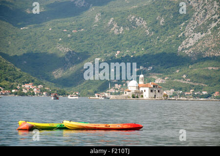 L'isola della Madonna della roccia nella Baia di Kotor con montagne calcaree in background con barche di fronte Foto Stock