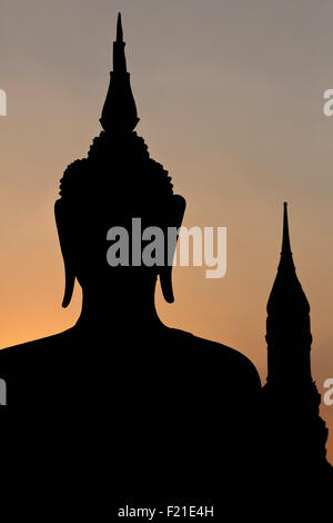 Thailandia Sukothai testa e le spalle del Buddha seduto e torre di sfondo stagliano contro il Cielo di tramonto Wat Mahathat Foto Stock