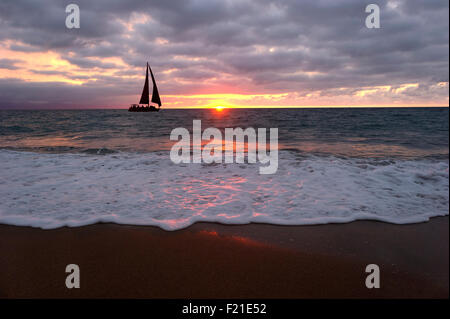 Barca a vela sunset silhouette è l'arancio brillante sole tramontare all'orizzonte mentre si profila una barca a vela si sposta lungo l'acqua come Foto Stock