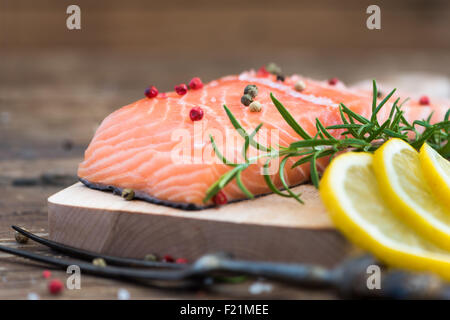 Salmone crudo Filetto di pesce con il limone, spezie e erbe aromatiche fresche sul tagliere pronto per cucinare Foto Stock