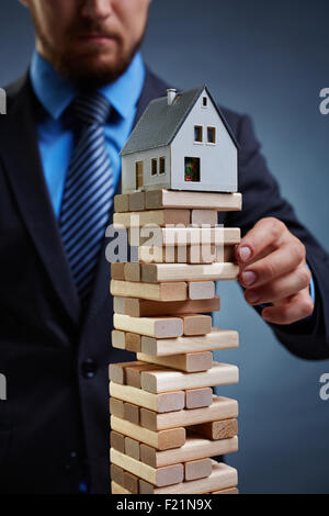 Imprenditore toccando torre da piccoli blocchi di legno con la casa sulla sua parte superiore Foto Stock