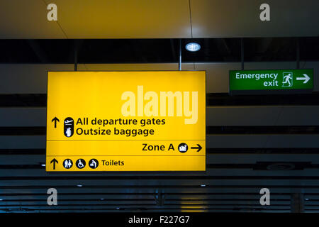 Partenza giallo segno verde e uscita di emergenza segno nella sala partenze dell'aeroporto internazionale di Heathrow, Londra Foto Stock