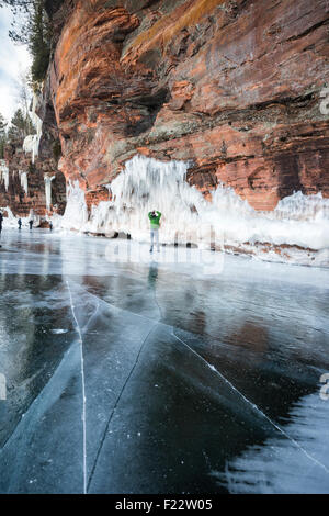 Uomo in piedi sul lago ghiacciato Superior guarda fino a ghiaccioli mentre visitano le grotte di ghiaccio a apostolo Island National Lakeshore, WI Foto Stock