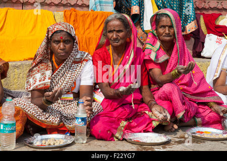 Pellegrini di tenere fuori le palme in attesa di ricevere prasad (il cibo come un religioso offrendo) sul ghats accanto al Gange a Varanasi Foto Stock