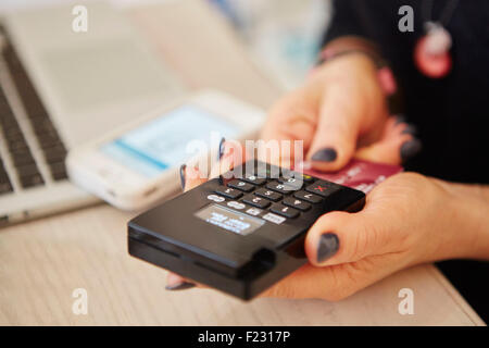 Una donna con le mani in mano in possesso di un lettore di carte di credito, l'elaborazione di pagamento o il pagamento per le merci. Foto Stock