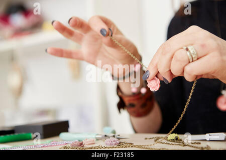 Una donna seduta su un banco da lavoro tenendo una catena d'oro con un piccolo telecomando floreali, la gioielleria. Foto Stock