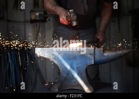 Un fabbro di formatura a caldo di un pezzo di ferro su una incudine con un martello, scintille con battenti. Foto Stock