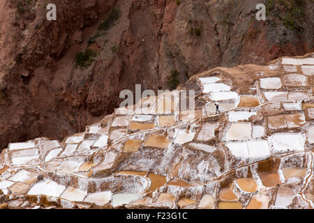 Il Perù, Maras, Lone lavoratore trasporta un carico tra sale di pool di evaporazione di Salineras nella Valle Sacra nelle montagne delle Ande Foto Stock