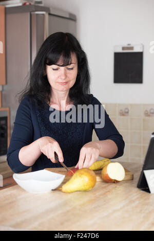 Donna sorridente affettamento apple in cucina sul tagliere per fare un cocktail di frutta Foto Stock